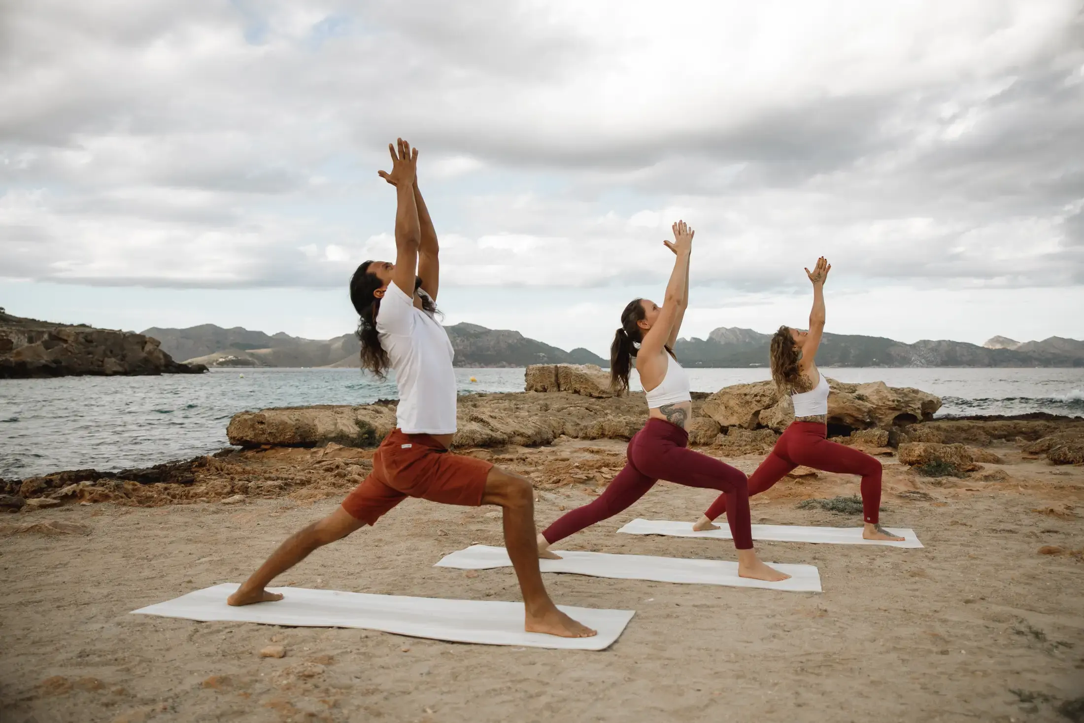 three people wearing identical yoga clothing doing the warrior yoga pose on the beach next to one another