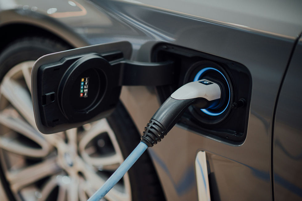 Electric car being charged, close-up of charging port and cable. Gray vehicle, blue accents, blurred wheel in background, modern feel.