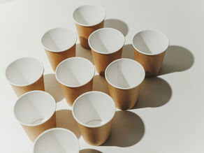 Ten brown paper cups arranged in a triangle on a white surface. Soft shadows and warm lighting create a minimalistic and clean mood.