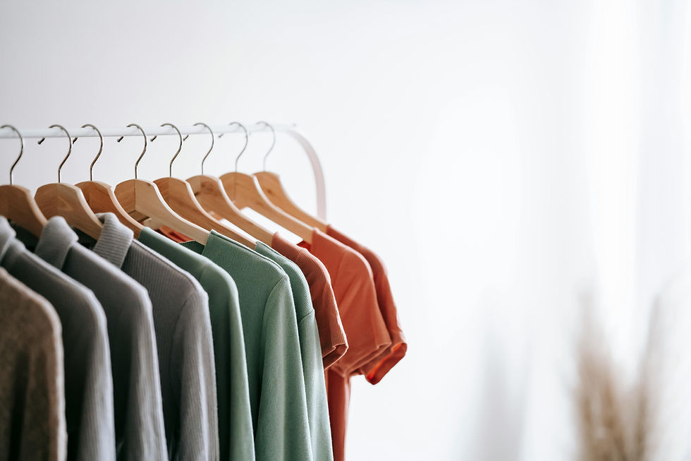 Clothes in various colors, including green and orange, hang on wooden hangers against a white background. Peaceful and organized setting.