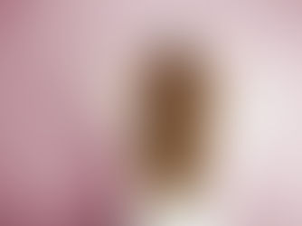 Person with long brown hair and white sweater holding their head, facing a pale pink wall. Hair appears wavy and smooth.