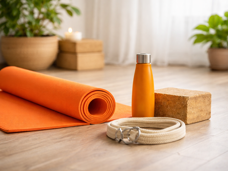 Orange yoga mat, yoga strap, orange waterbottle and tan yoga block in a lit studio.