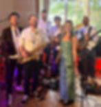 Wedding Band Jemima & The Five in a function room with large window, woman in green zebra dress, men with instruments, relaxed vibe, colorful lighting and decor.