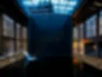 Indoor pool with a glass ceiling; a person is swimming under a water stream. Dimly lit, modern ambiance with lanterns on the deck.