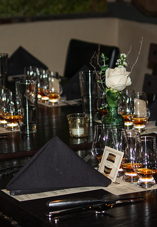 Elegant banquet table setup at Elbow Room in Fresno, featuring black linens, whiskey tasting glasses, a single white rose