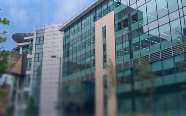 Modern corporate building with glass facade, reflecting sky and trees.