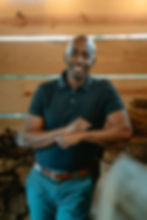 Smiling man in a dark blue shirt leans against wood pile