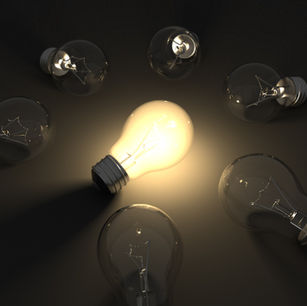 Lit lightbulb surrounded by unlit light bulbs on the floor in a dark room