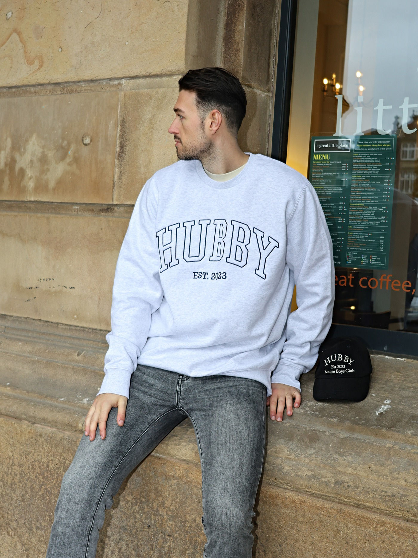 Man sitting against a stone building wearing a grey sweatshirt