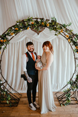 Wedding photographer under wedding arch with wife and baby
