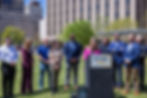 Councilor Gilbert speaking at a podium with other councilors and the mayor behind her.