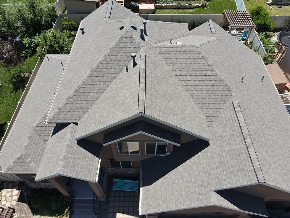 Overhead view of a gray shingle roof with ridges, vents, and intersecting roof slopes.