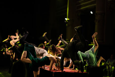 Many dancers hopping their feet in the air, while holding themselves to the table in front of them.