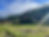 Thatched-roof houses beside a green rice field in a misty mountain village, with bright sunbeams and blue sky above.