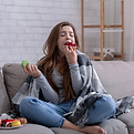 Sad young lady coping with depression or stress by eating sweets on sofa at home. Unhappy