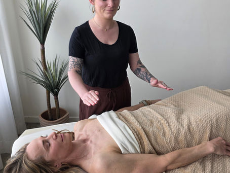 A Massage Therapist holding her hands above a woman lying down, performing energy healing.
