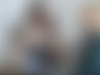 Two women sitting and smiling, one holding a tablet. Books on sports medicine in the background. Bright room, friendly atmosphere.