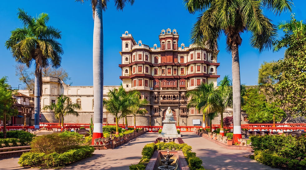 Ornate palace-like building with palm trees and a central statue in a sunny garden under a bright blue sky.