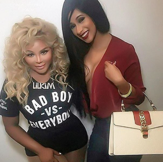 Two female rap artists pose together against a plain background, smiling at the camera. One wears a black “Bad Boy vs Everybody” t-shirt with voluminous blonde hair, while the other wears a deep red blouse and holds a structured handbag.