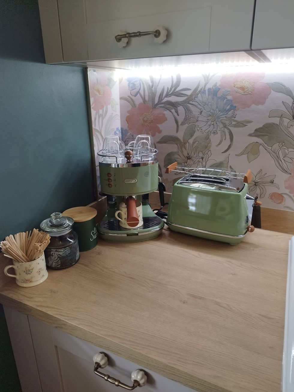 Coin petit-déjeuner dans la cuisine - Petite cuisine avec machine à café et grille-pain verts sur un plan de travail en bois. Fond floral, ambiance rétro chaleureuse.