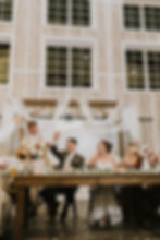 Bride and groom smiling and raising glasses as they toast during the best man’s speech, surrounded by guests at their Minnesota wedding reception.