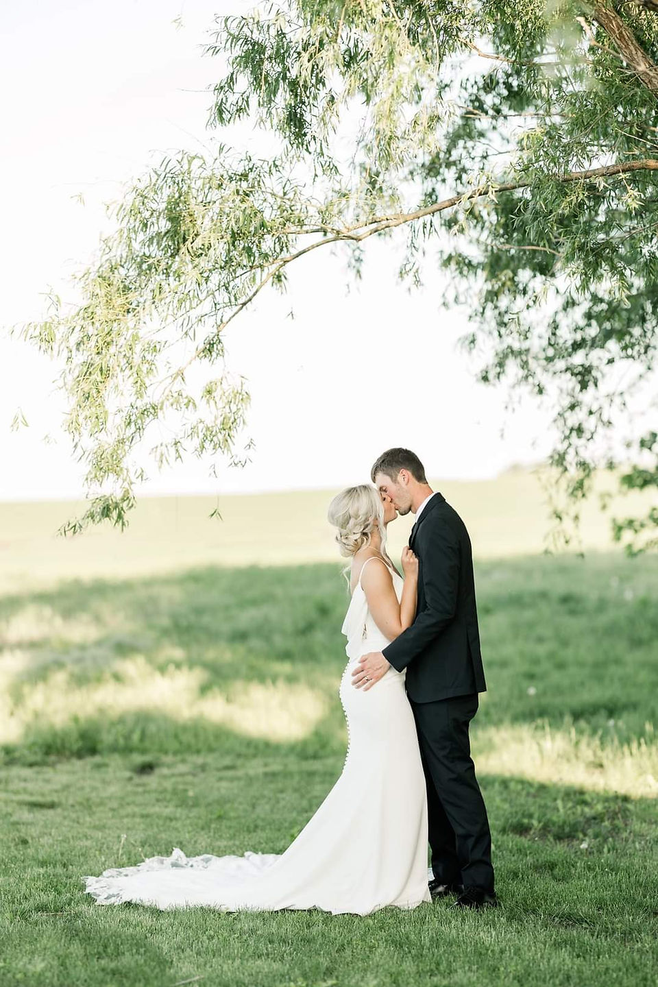 Bride and groom kissing in prairie grass with trees in the background at Southwest Minnesota rustic wedding venue.