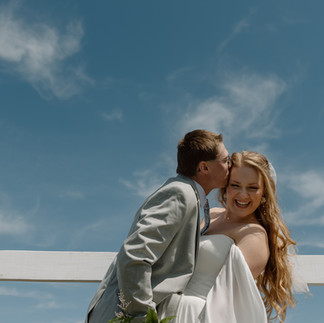 Groom sneaks a kiss from his bride along the white fence at 5 Family Ranch, a candid moment captured by a Minnesota wedding photographer.