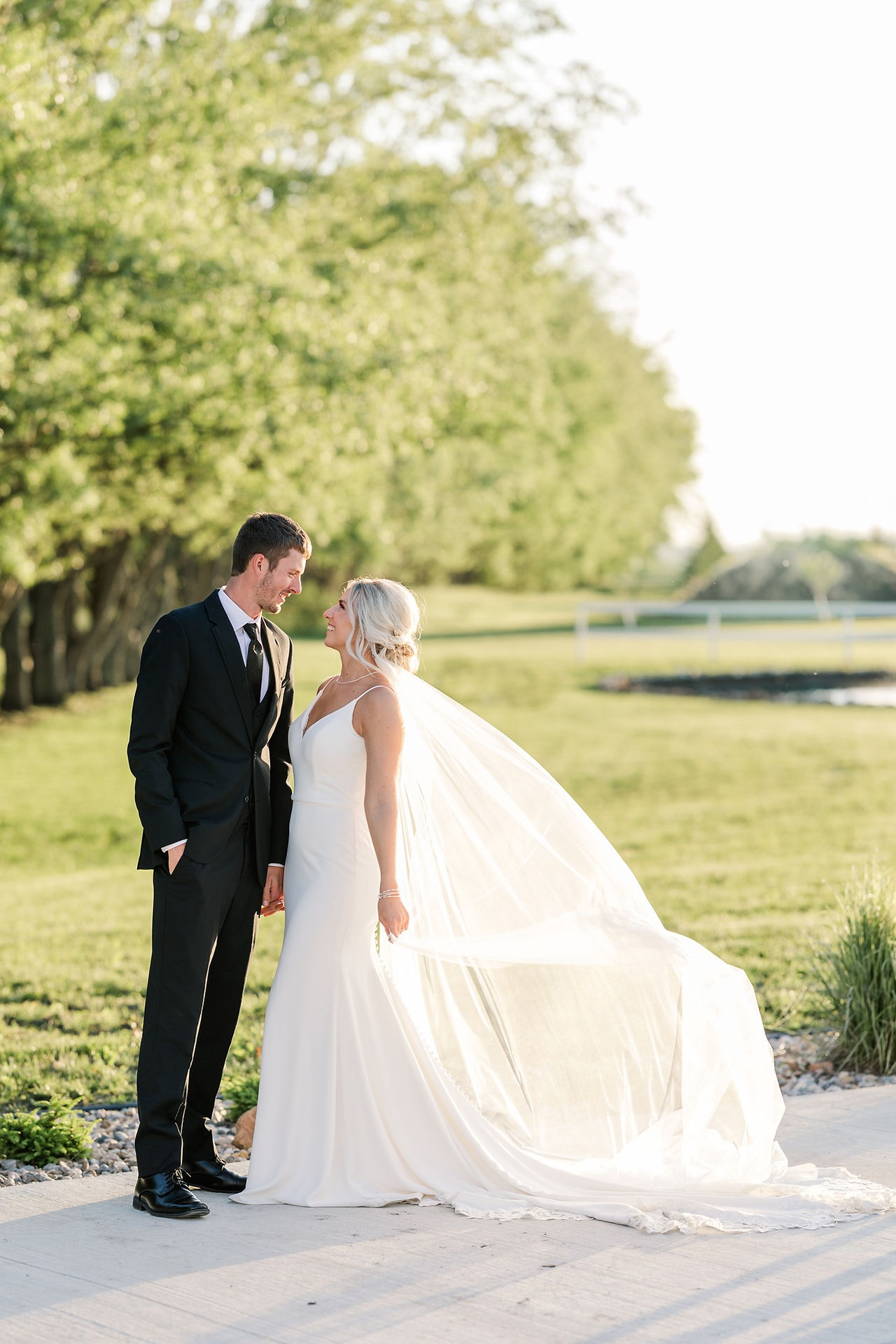 Bride and groom gazing at each other with pond and golden sunset behind them at Minnesota wedding venue.