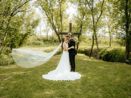 Bride and groom sharing a kiss in the trees, with a cross in the background, captured by Minnesota wedding photographer Skye Photography.