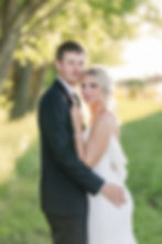 Bride and groom holding each other, smiling at camera with sunset glowing behind them at Marshall MN wedding venue.