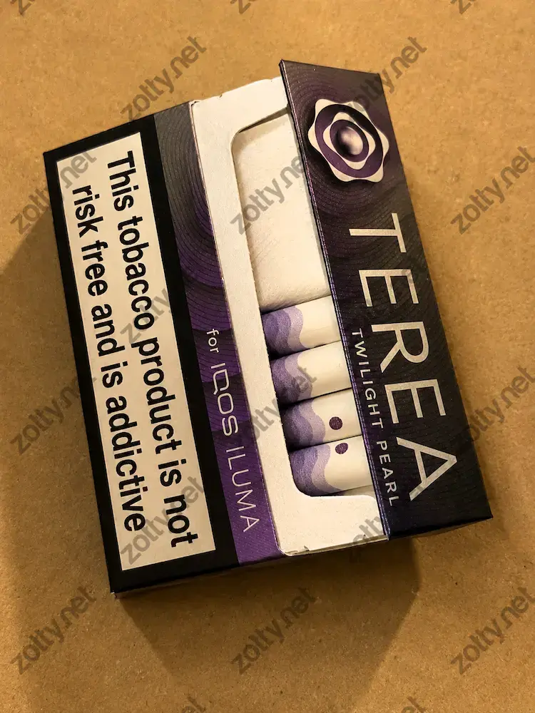 Close-up of a purple Terea Twilight Pearl tobacco pack with a health warning label, resting flat on a plain cardboard surface.