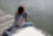A young woman sitting on a dock and looking at the lake while thinking.