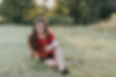 Young woman smiling and sitting in a grassy field.