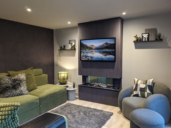 Garden annexe living room with green sofa, TV media wall, electric fire and floating shelves in Gloucestershire