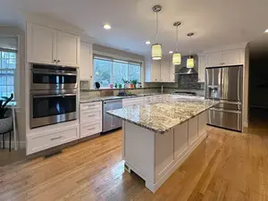 A large kitchen featuring white cabinets and a central island, recently remodeled with cabinet refacing.