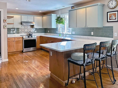 A two-tone kitchen in Hudson, NH, featuring a large island with bar stools, agave upper cabinets, and honey-stained base cabinets.