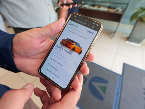 Tela de smartphone exibindo informações digitais de um veículo ao lado de um carro estacionado, simbolizando o Passaporte Veicular Digital baseado em blockchain.