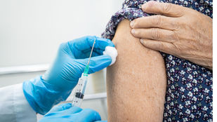 Profissional de saúde com luvas azuis aplica vacina no braço de uma pessoa idosa