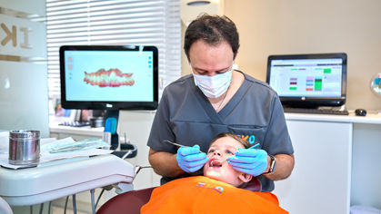 Criança sorrindo durante consulta odontológica, com aparelho dentário infantil, representando o tratamento ortodôntico precoce.