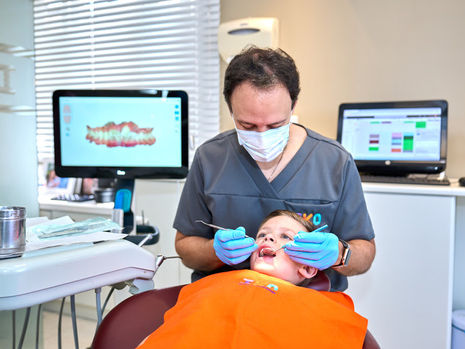 Criança sorrindo durante consulta odontológica, com aparelho dentário infantil, representando o tratamento ortodôntico precoce.
