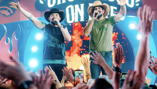 Estrutura do evento Churrasco On Fire com churrasqueiros, Máquina do Churrasco e público reunido, representando a experiência gastronômica e musical criada por Fernando e Sorocaba.