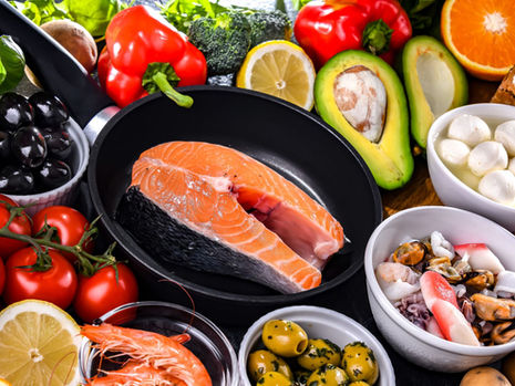 Posta de salmão em uma frigideira cercada por tomates, azeitonas, abacate, pimentões, limão, laranja, pão integral, queijo e frutos do mar