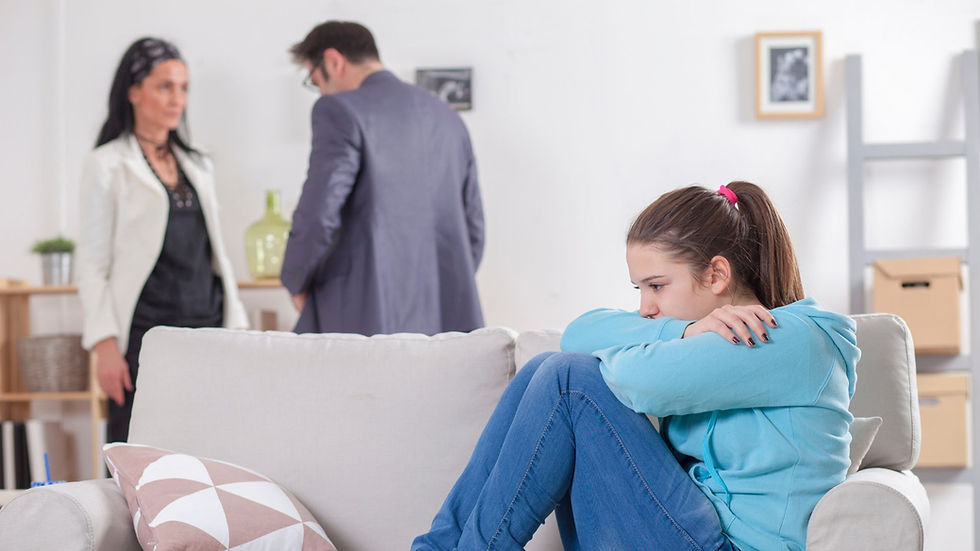 Menina sentada no sofá, abraçada aos joelhos e de cabeça baixa, enquanto um casal discute ao fundo da sala