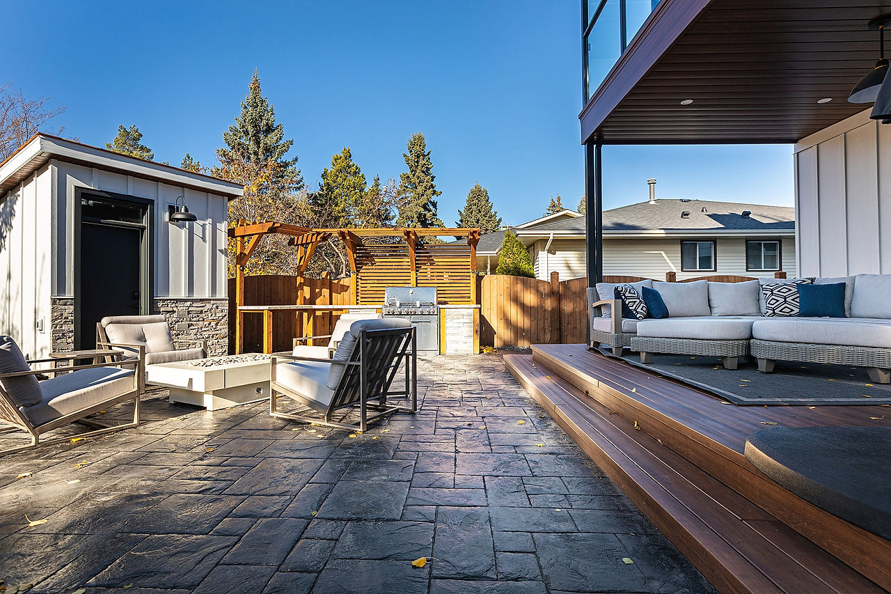 Raised wooden deck leading to a stone backyard patio firepit