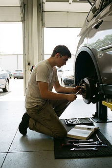 General service automotive technician performing routine vehicle repairs in service bay.