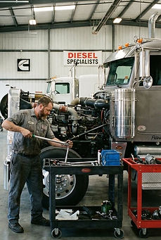 Diesel automotive technician working on heavy-duty truck in service facility.