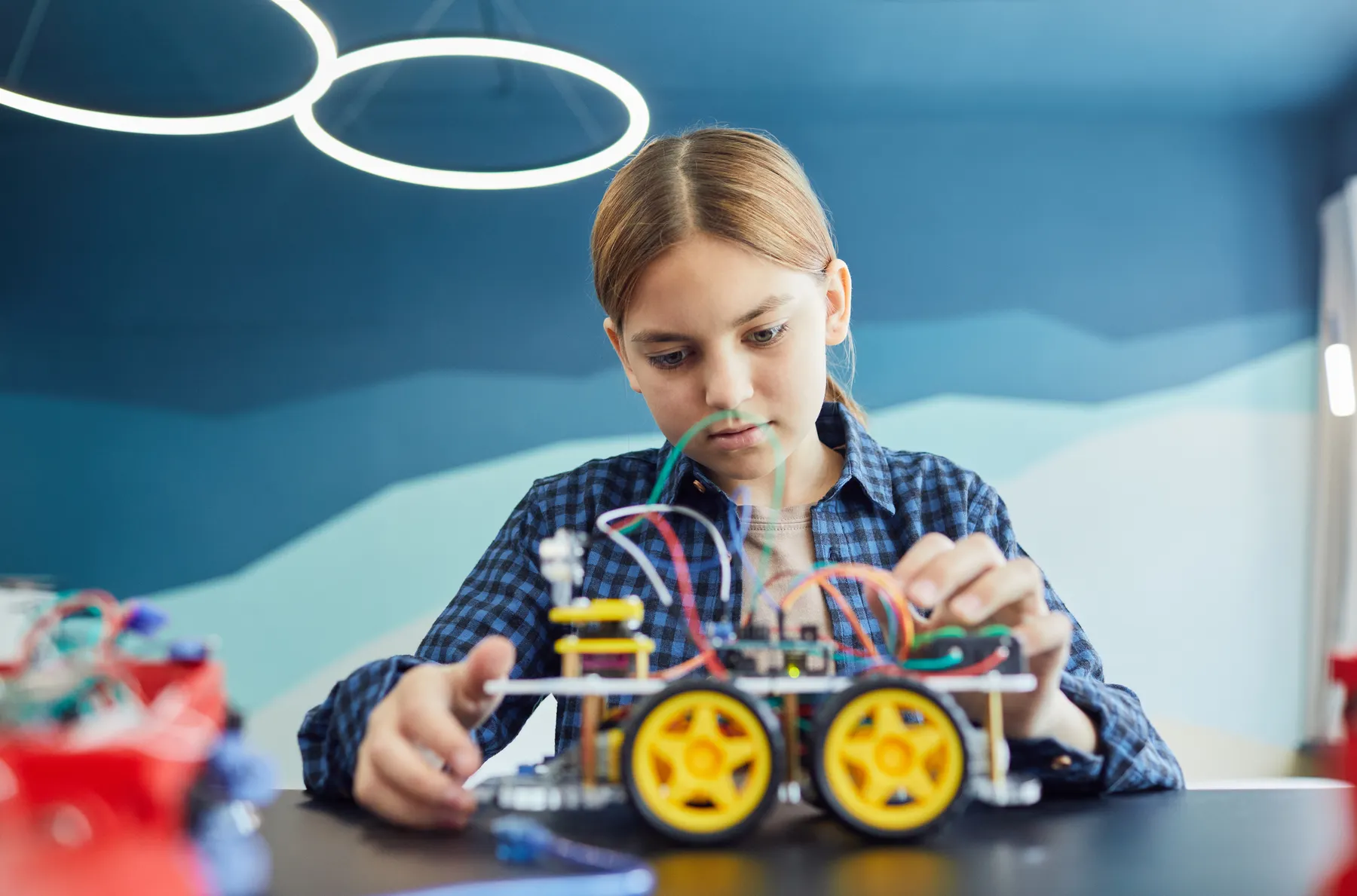 A student examines a wheeled robot with exposed wires.