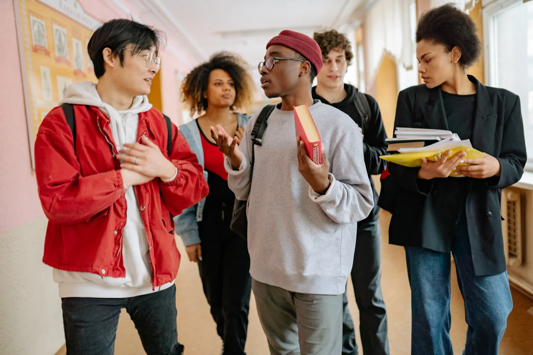 Students with books walk and talk together in a corridor.