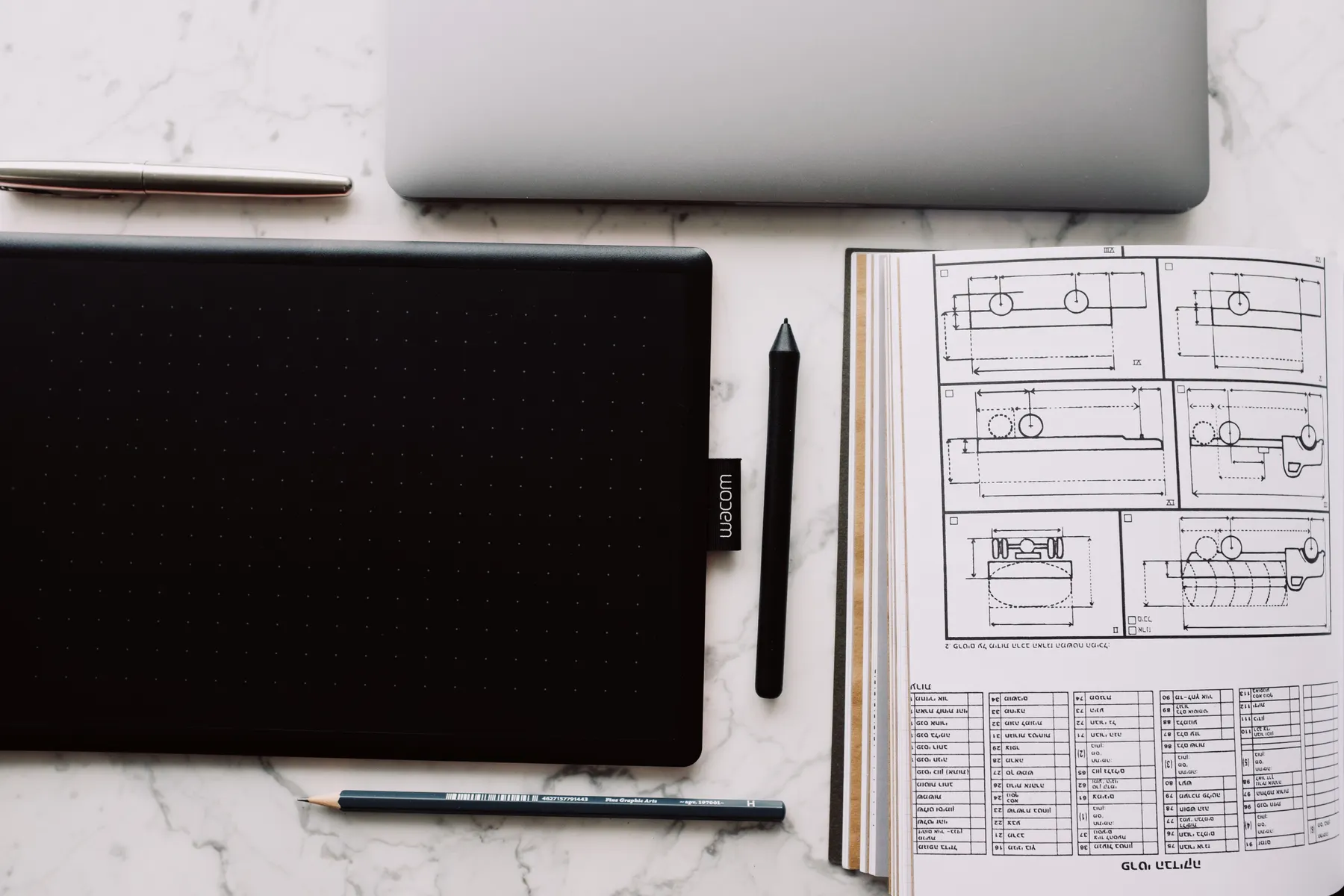 A rough technical sketch lies beside a tablet and laptop.
