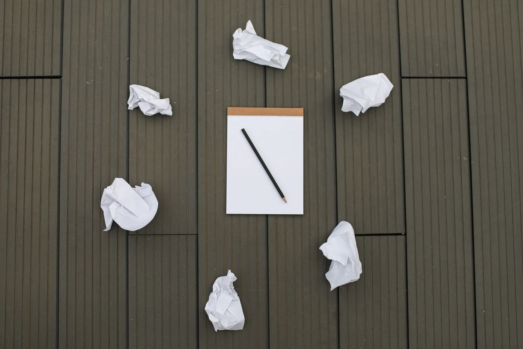 Crumpled paper sits beside a blank notebook and pencil.